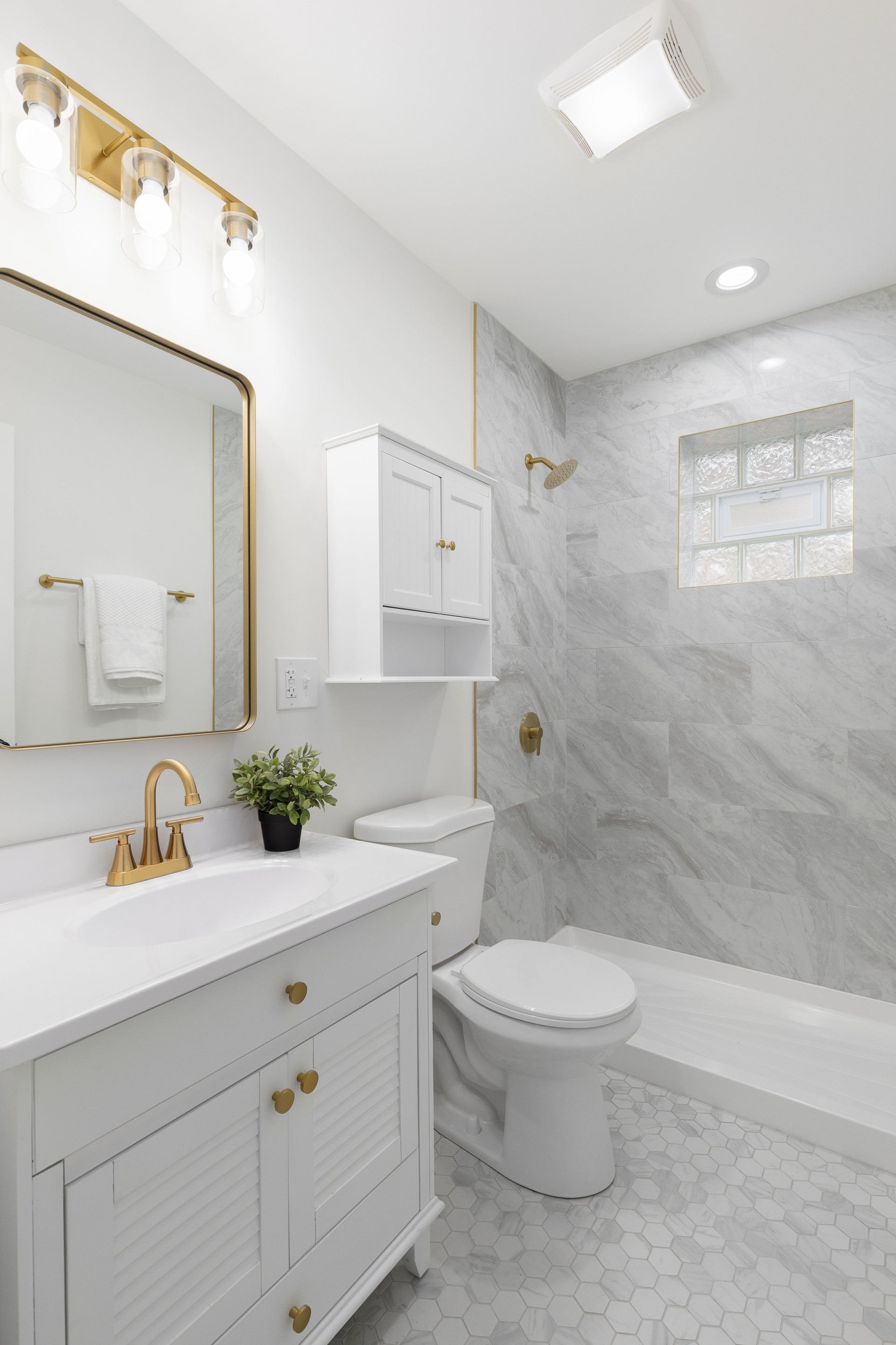 A white bathroom with gold accents and marble tiled shower and floor.